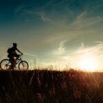 Person fährt bei Sonnenuntergang locker Fahrrad über ein Feld, aktive Erholung am Ruhetag