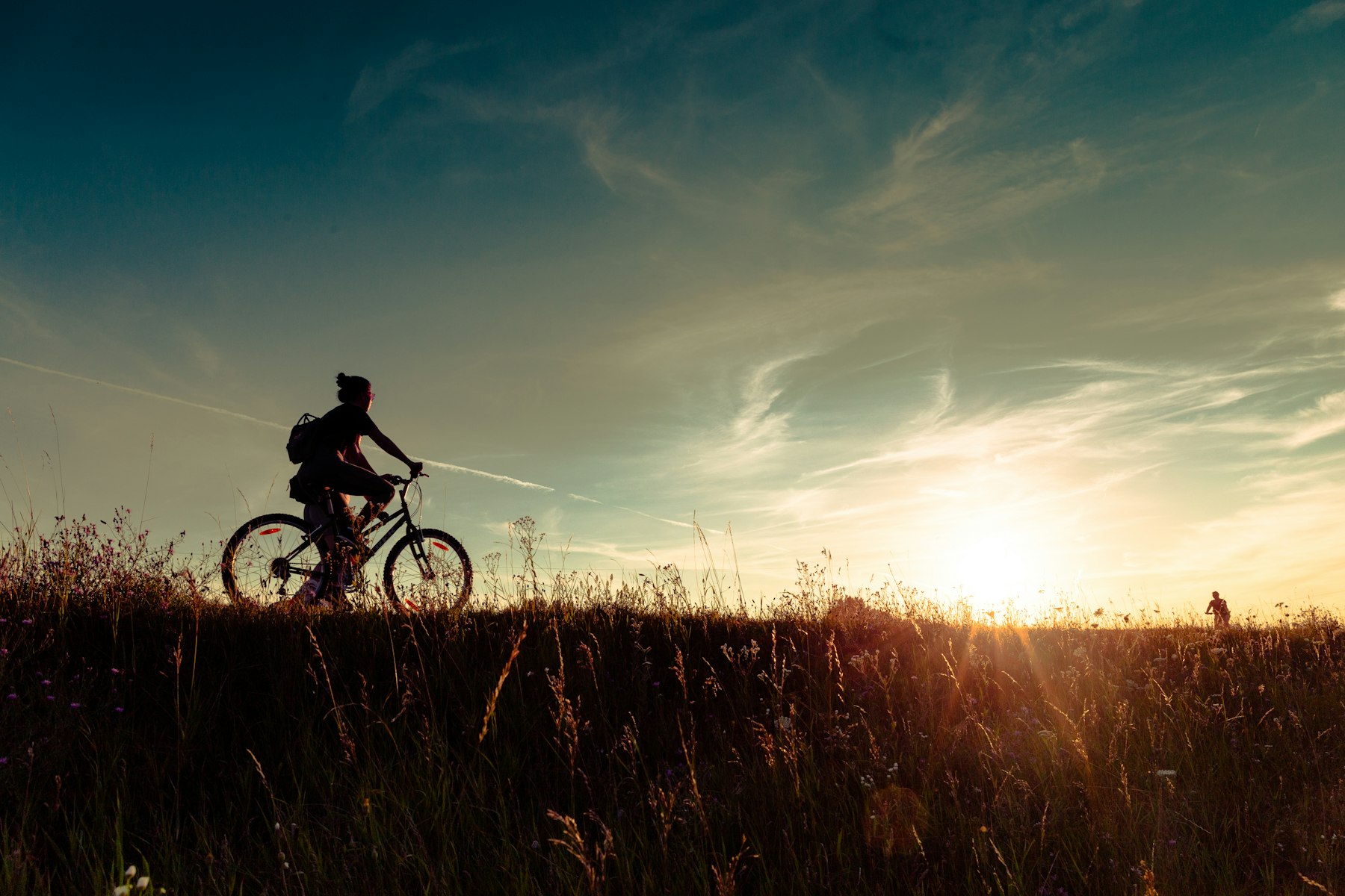 Person fährt bei Sonnenuntergang locker Fahrrad über ein Feld, aktive Erholung am Ruhetag