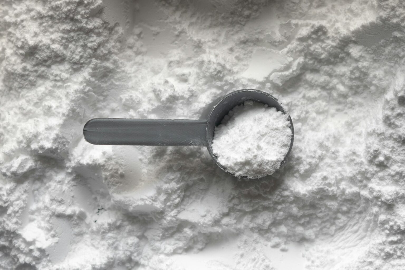 Kreatin: grauer Messlöffel mit weißem Kreatinpulver