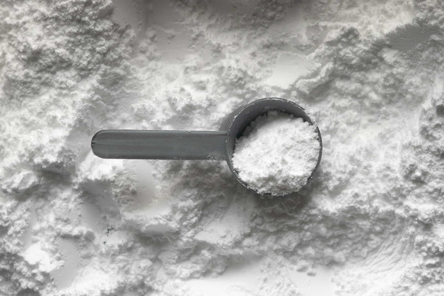 Kreatin: grauer Messlöffel mit weißem Kreatinpulver