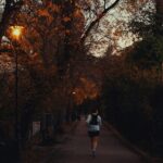 Läufer in Laufkleidung für den Herbst auf baumgesäumtem Parkweg in der Abenddämmerung