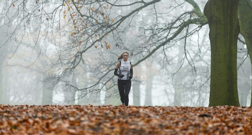 Läuferin in langer Laufkleidung joggt am kühlen Morgen unter kahlen Bäumen durch einen Park