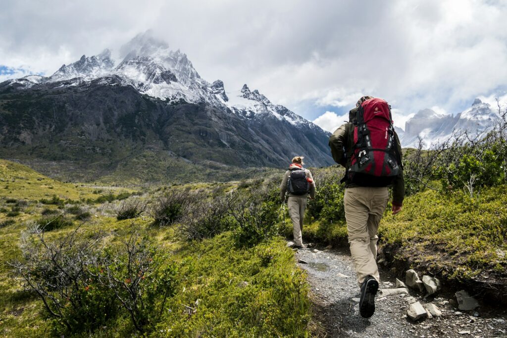Zwei Wandernde mit Wanderrucksack auf einem Pfad Richtung schneebedeckter Berge