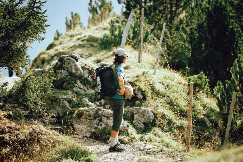 Wanderer mit Tagesrucksack rastet an einem felsigen Bergpfad zwischen Kiefern