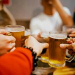 Freunde stoßen mit Biergläsern an, Symbolbild für Alkohol und Muskelaufbau