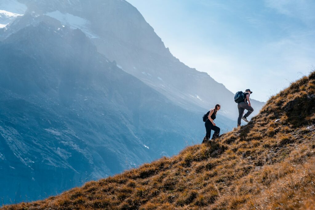 Zwei Wanderer steigen auf einem steilen Grashang auf, Bergwanderung in den Schweizer Alpen