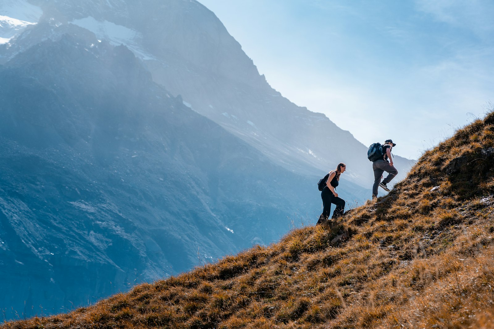 Zwei Wanderer steigen auf einem steilen Grashang auf, Bergwanderung in den Schweizer Alpen