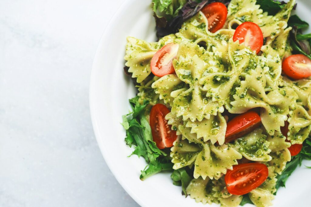 Teller mit Pesto-Nudeln und aufgeschnittenen Tomaten auf einem hellen Tisch