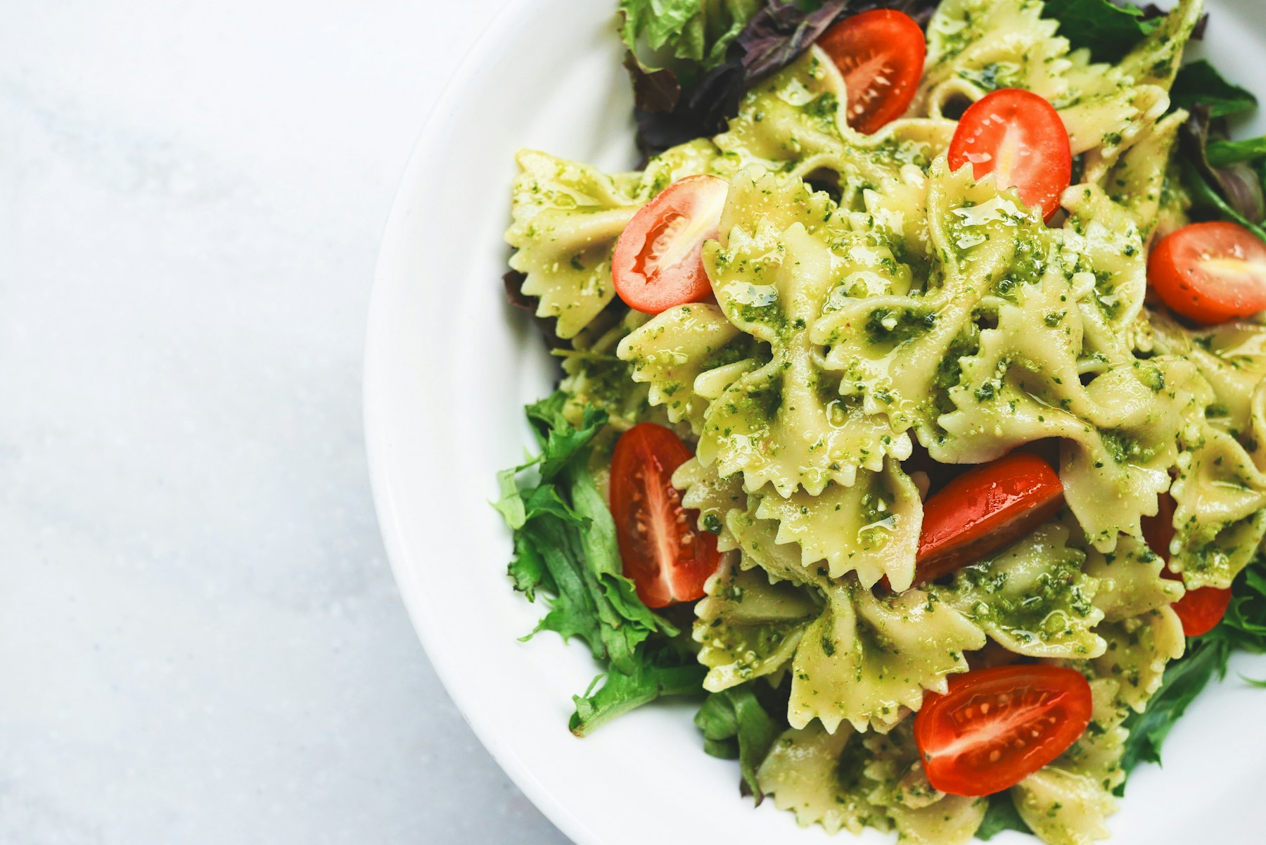 Teller mit Pesto-Nudeln und Tomaten als typische Mahlzeit beim Carboloading vor einem Wettkampf