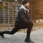Dynamisches Dehnen vor dem Lauf: Läufer in Winterkleidung mobilisiert sich im Park