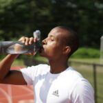 Sportler trinkt aus einer schwarzen Sportflasche, um Flüssigkeit und Elektrolyte nach dem Training aufzufüllen