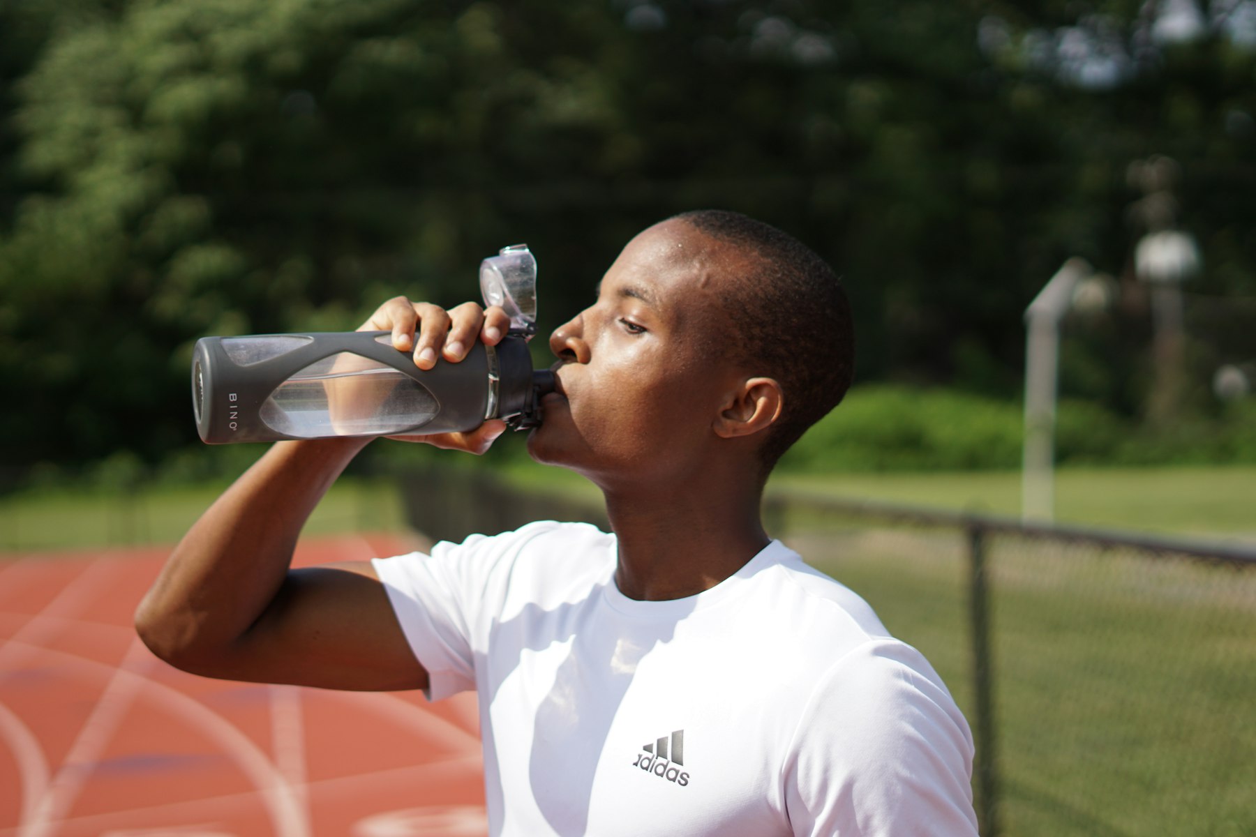 Sportler trinkt aus einer schwarzen Sportflasche, um Flüssigkeit und Elektrolyte nach dem Training aufzufüllen