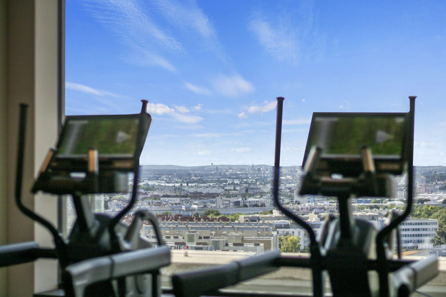 Zwei Ellipsentrainer vor einer großen Fensterfront mit Blick auf eine Stadt