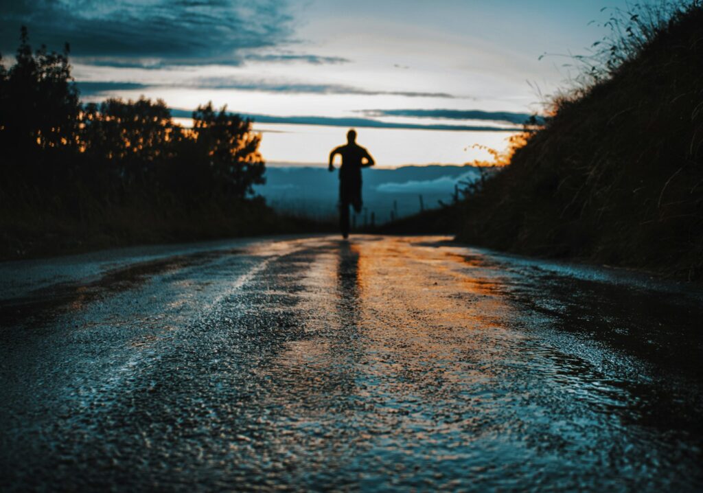 Silhouette einer Person beim Morgenlauf auf einer Straße im Gegenlicht