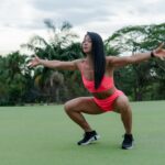 Frau in pinker Trainingskleidung macht beim Ganzkörpertraining im Freien eine tiefe Kniebeuge