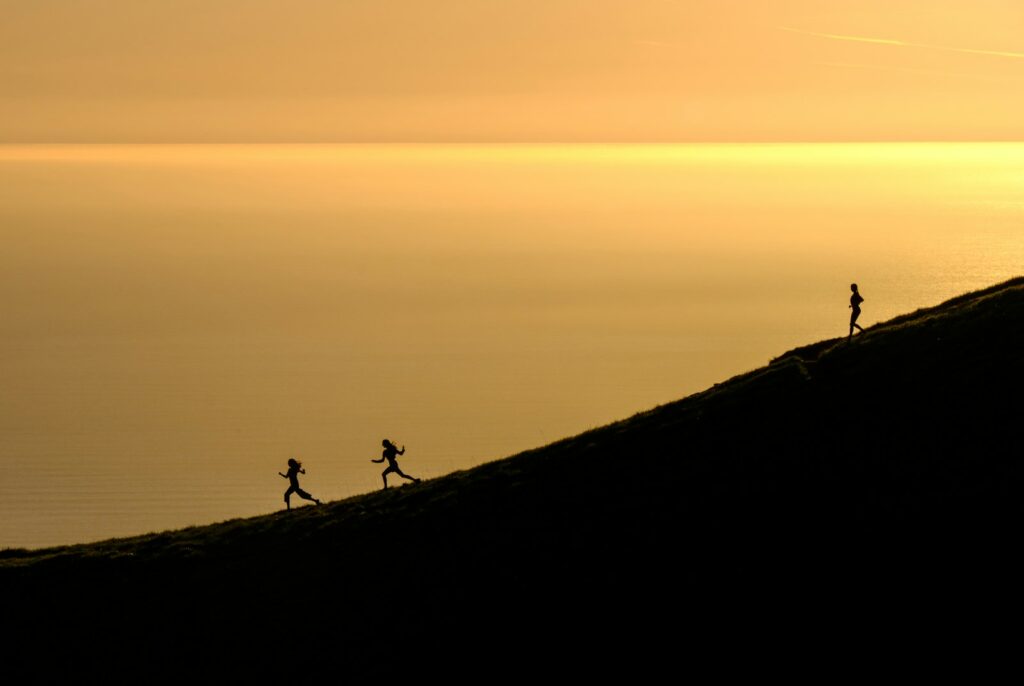 Drei Läufer laufen in der Abendsonne locker einen Hügel hinab, wie in der Trabpause nach Bergintervallen