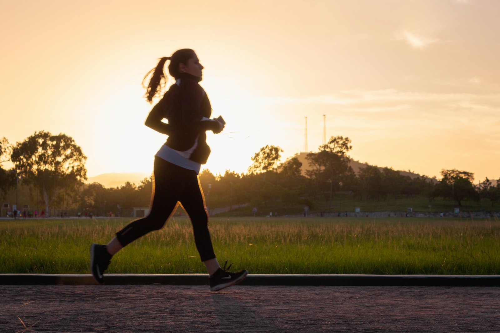 Joggen Vorteile: Läuferin als Silhouette auf einem Weg im goldenen Abendlicht