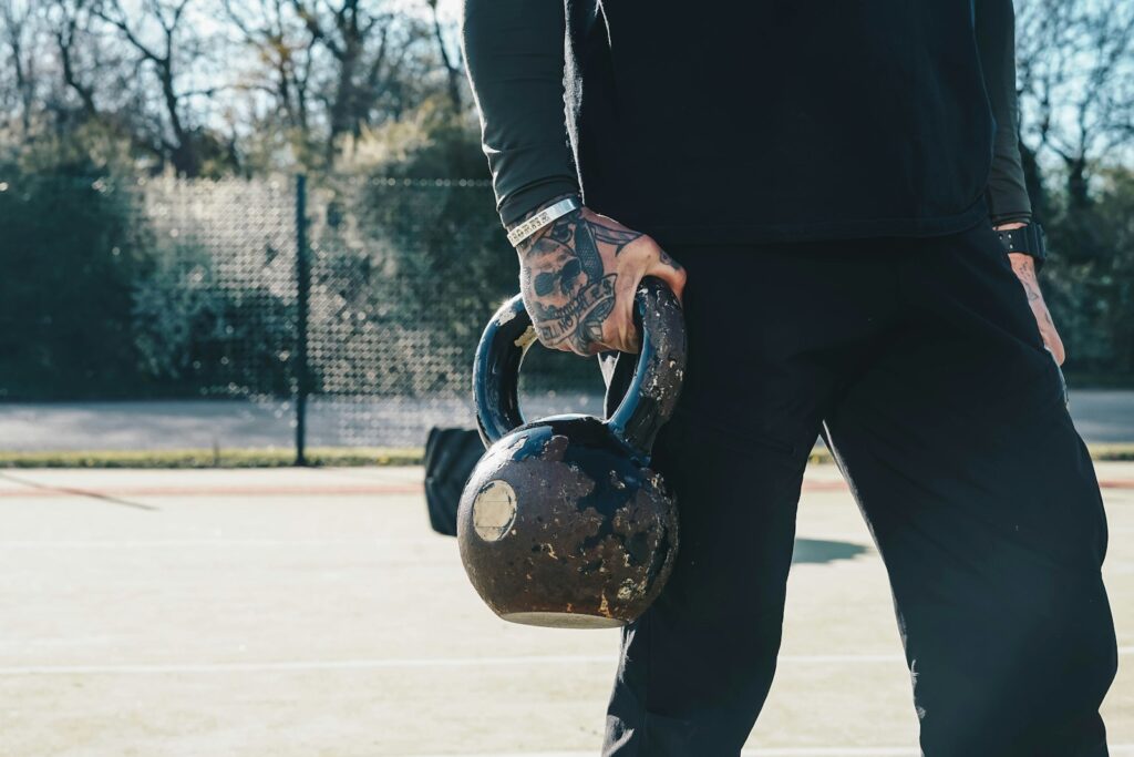 Mann trainiert im Freien auf einem Sportplatz mit einer Kettlebell