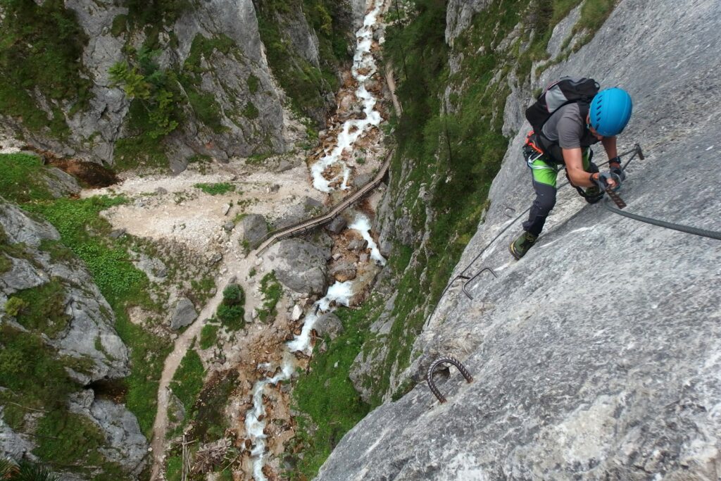 Bergsteigerin mit kompletter Klettersteig-Ausrüstung am Drahtseil eines Klettersteigs in den Alpen
