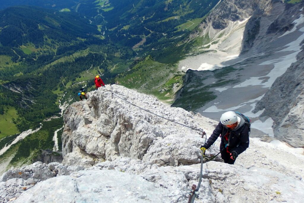 Drei Personen mit Helm und Klettersteigset an einem Klettersteig in einer Felswand