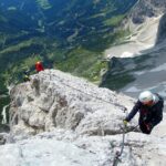 Drei Personen mit Helm, Gurt und Klettersteigset als Klettersteig-Ausrüstung in einer Felswand