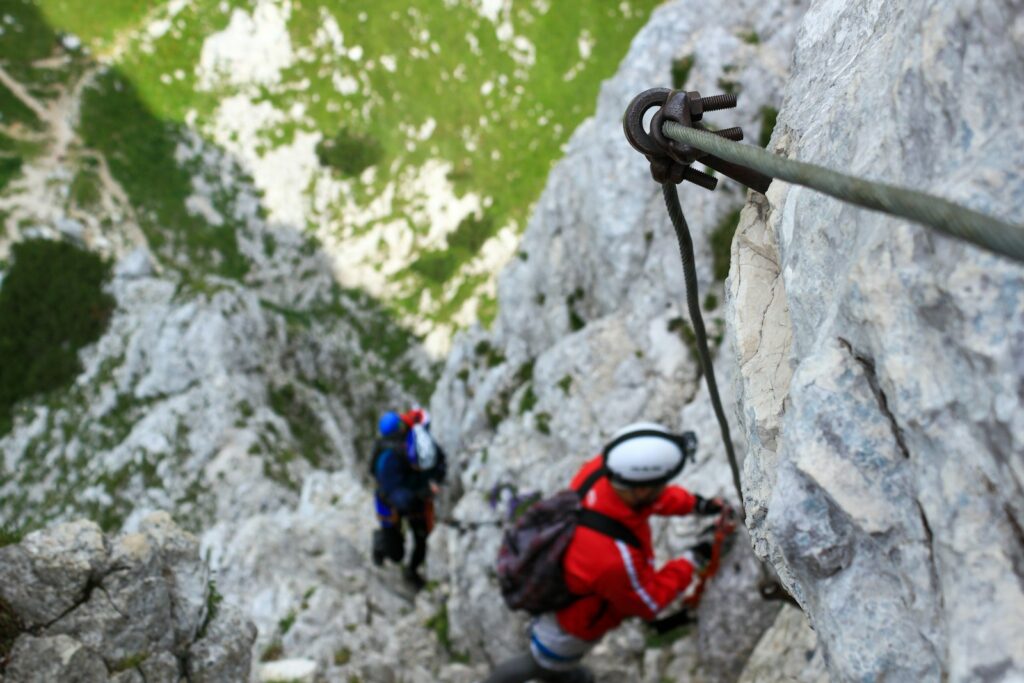 Bergsteiger am Stahlseil eines Klettersteigs blickt im grauen Fels nach unten