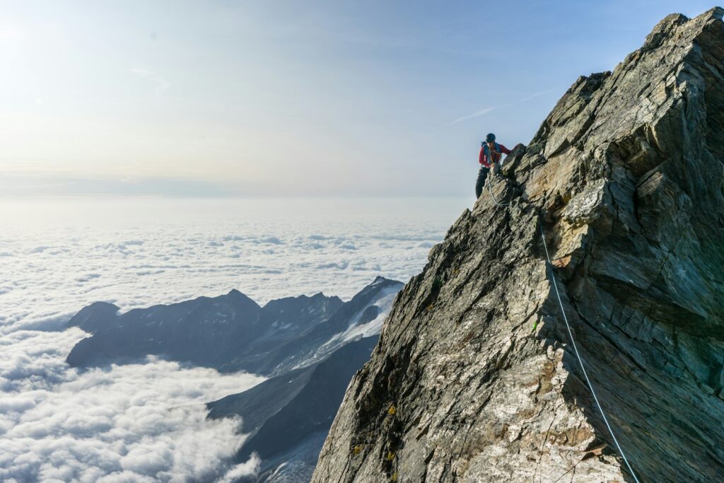 Bergsteiger mit Seil auf einem ausgesetzten Felsgrat über einem Wolkenmeer