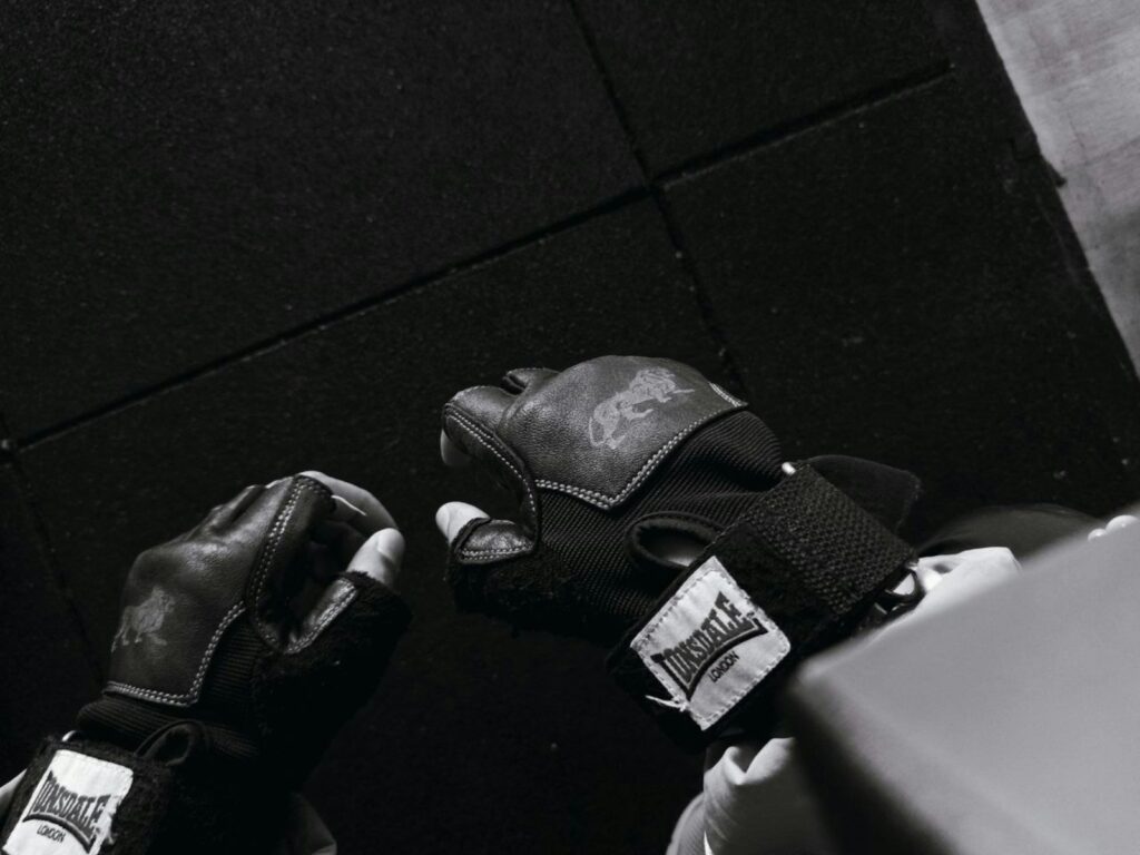 Hände mit fingerlosen schwarzen Krafttraining-Handschuhen aus Leder mit Handgelenkband