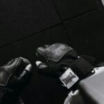Hände mit fingerlosen schwarzen Krafttraining-Handschuhen aus Leder mit Handgelenkband