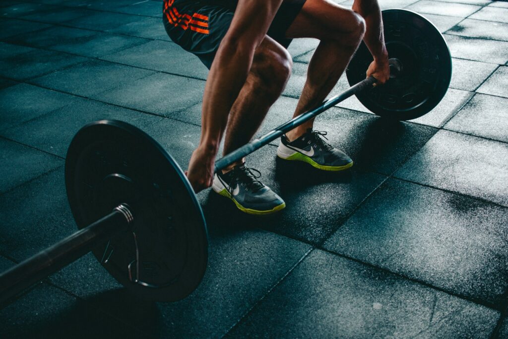 Person greift im Fitnessstudio eine beladene Langhantel, kurz bevor sie das Gewicht vom Boden hebt