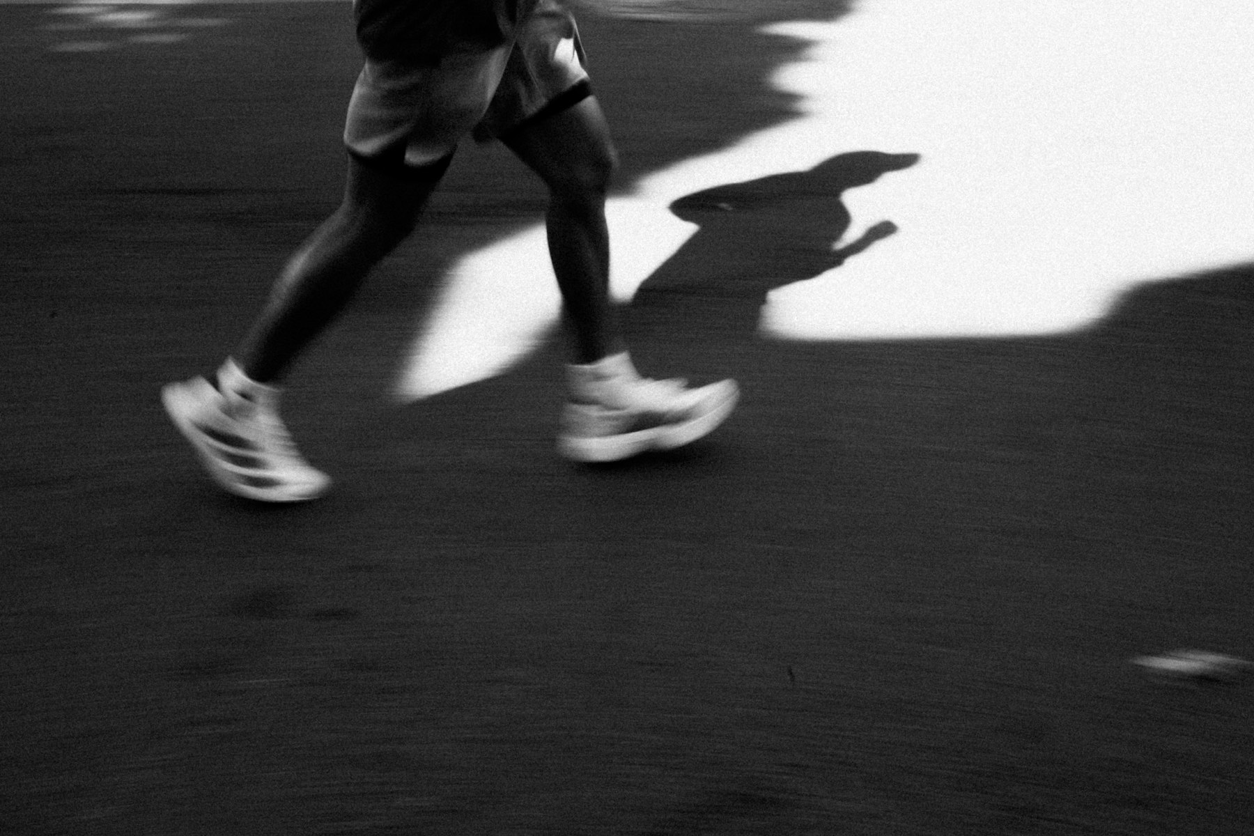 Beine einer laufenden Person in Laufschuhen mit langem Schatten, Fußbewegung und Pronation im Abrollen