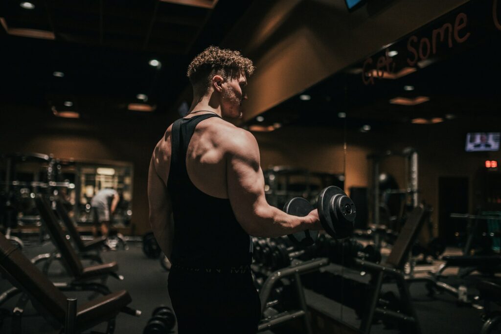 Mann hält im Fitnessstudio eine Kurzhantel, langsames Absenken von Gewichten löst oft Muskelkater aus