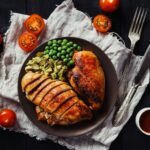 Hähnchenbrust mit Erbsen auf dunklem Teller als Beispiel für eine Mahlzeit, die den Proteinbedarf im Kraftsport unterstützt