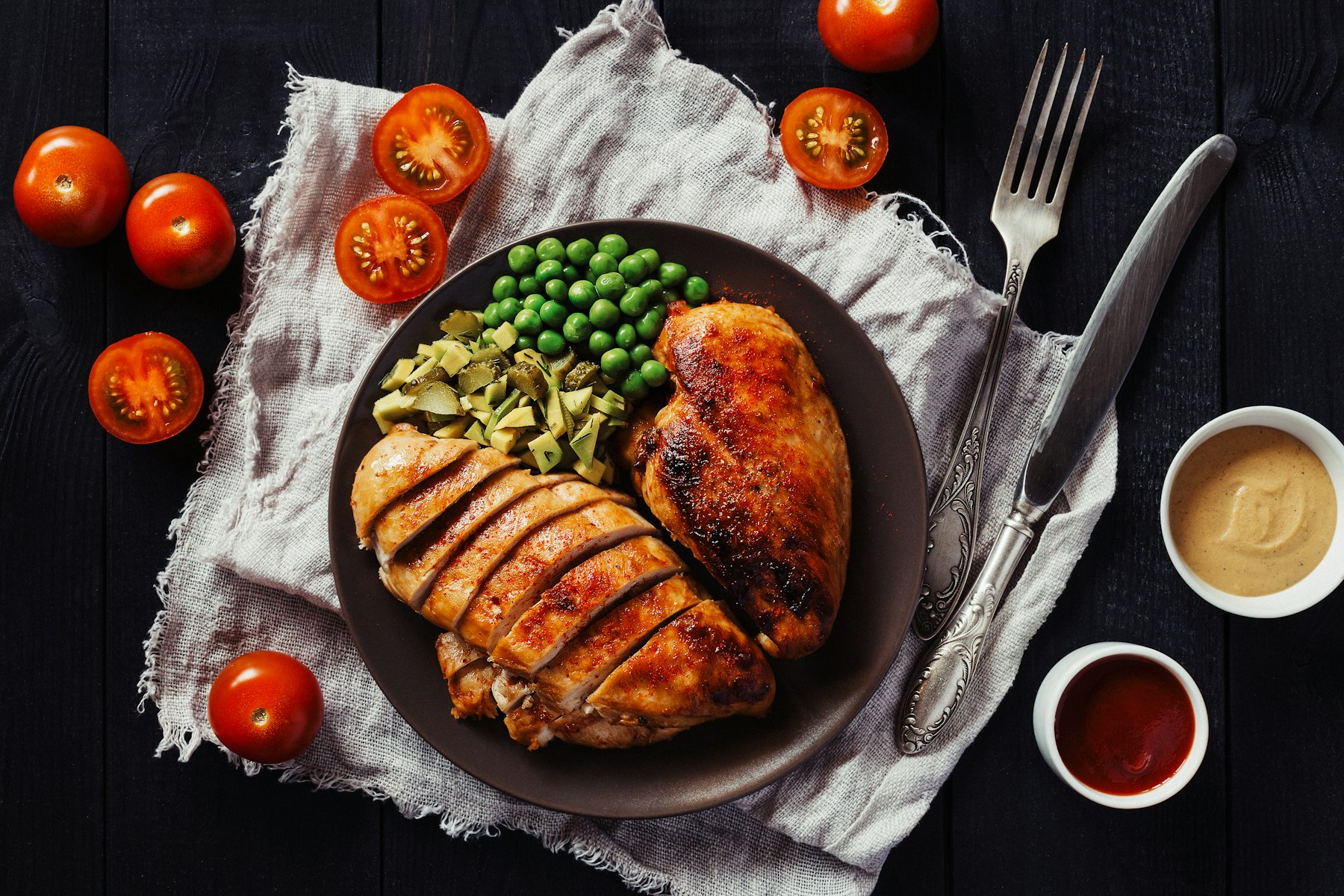 Hähnchenbrust mit Erbsen auf dunklem Teller als Beispiel für eine Mahlzeit, die den Proteinbedarf im Kraftsport unterstützt