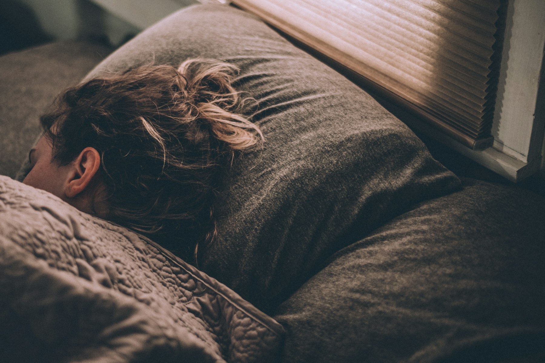 Frau schläft entspannt im Bett, Morgenlicht fällt durchs Fenster, Schlaf und Regeneration