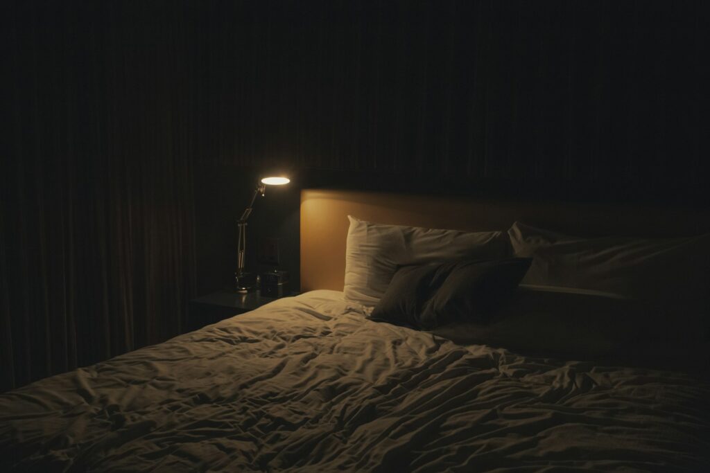 Gedimmte Nachttischlampe neben einem gemachten Bett als ruhige Abendroutine für besseren Schlaf