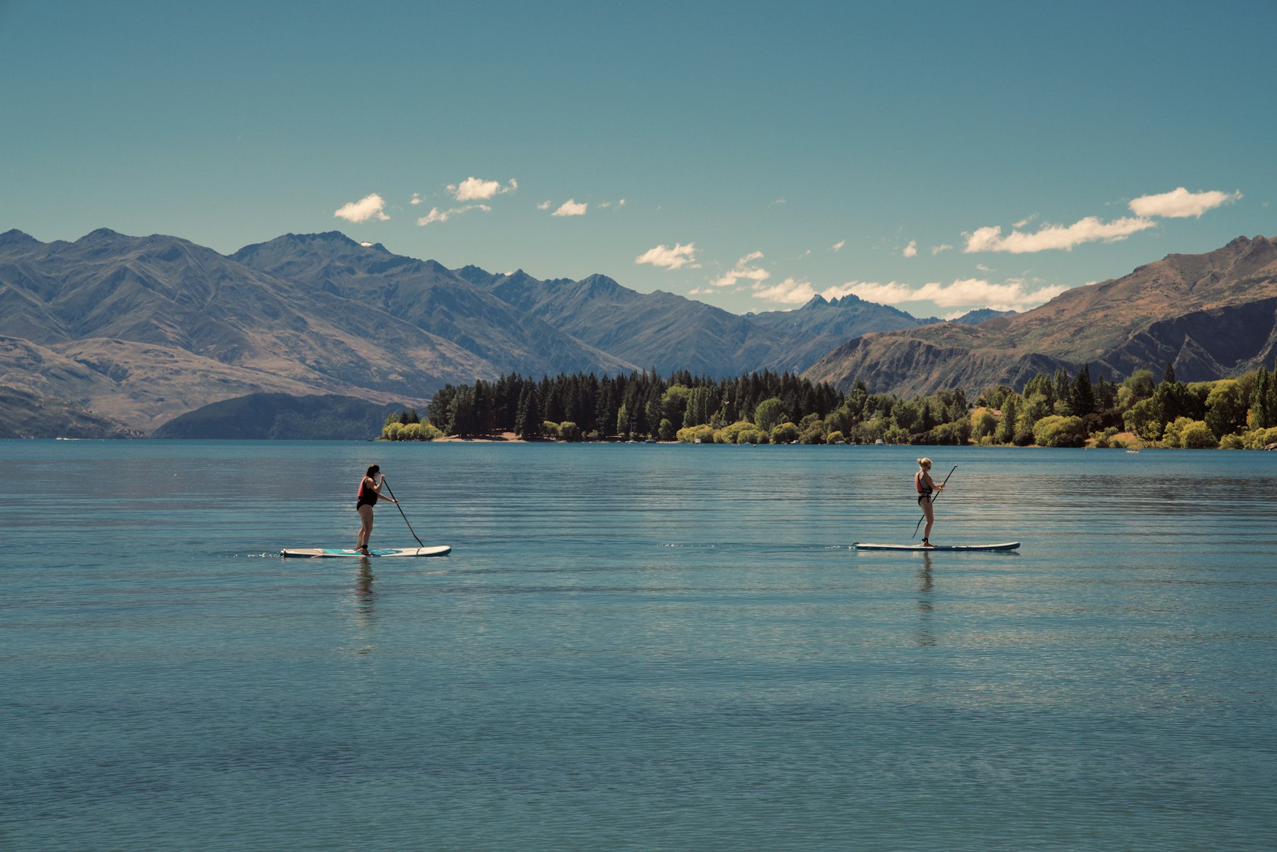 Zwei Personen zeigen ihre SUP-Paddeltechnik auf Boards auf einem See vor Bergen