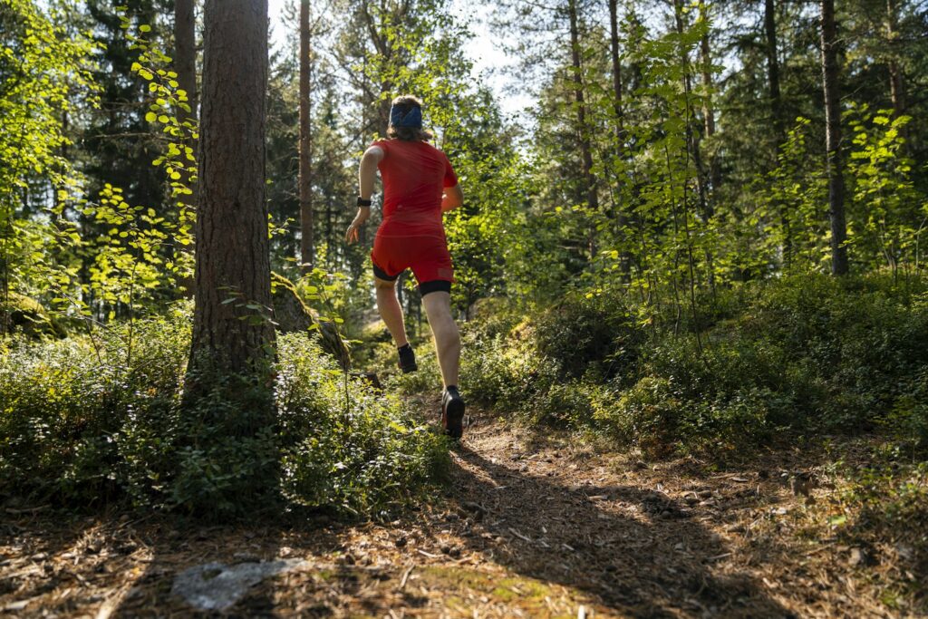 Läufer in roter Jacke läuft auf einem weichen Waldpfad zwischen Bäumen