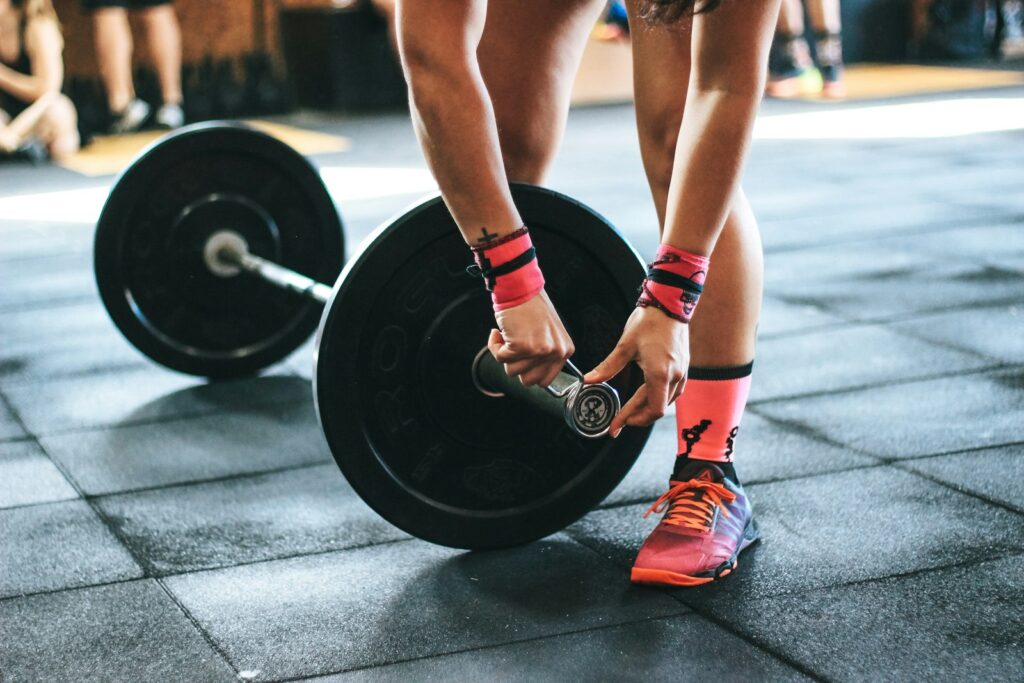 Hantelscheiben werden an einer Langhantel fixiert, Grundlage für den Trainingsplan Muskelaufbau mit Progression